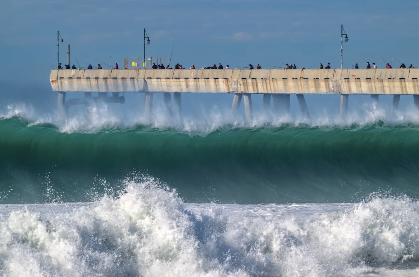 Large waves breaking at the Pacifica Pier with people watching from above